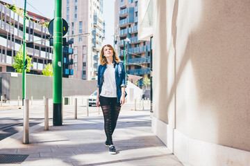 Young beautiful caucasian blonde hair gilr walking outdoor in the city, overlooking pensive