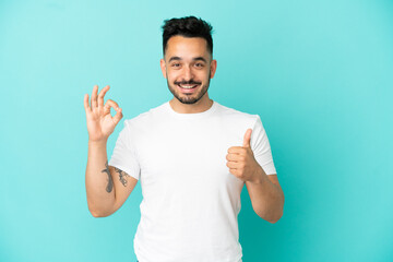 Young caucasian man isolated on blue background showing ok sign and thumb up gesture