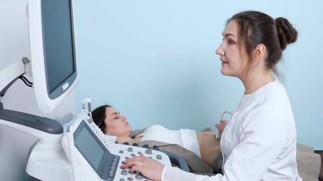 Smiling female doctor with hair bun does ultrasonography of abdominal organs to young woman with modern equipment in hospital office close view