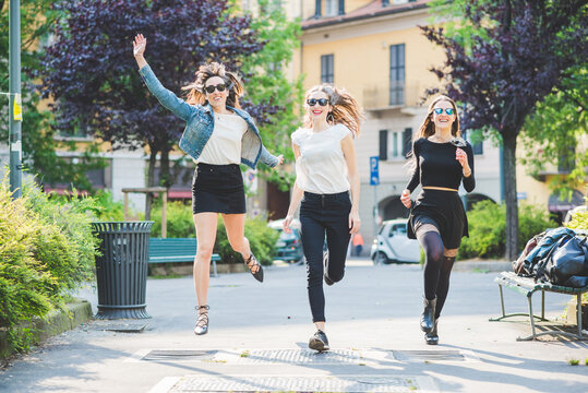 Three young beautiful cacuasian women millennials outdoor in the city running and jumping having fun smiling