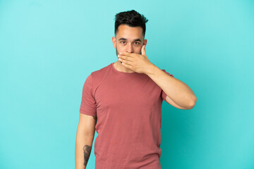 Young caucasian man isolated on blue background covering mouth with hand