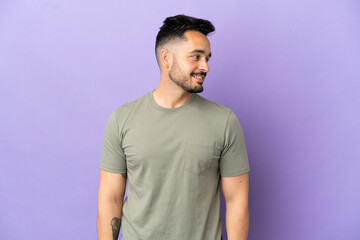 Young caucasian man isolated on purple background looking side