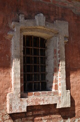 Close-up of a window with a metal grate. A red brick window in the wall of the monastery.