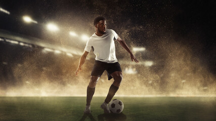 Professional male football, soccer player on stadium background. African fit athlete practicing, playing excited