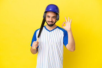 Young caucasian man playing baseball isolated on yellow background showing ok sign with fingers