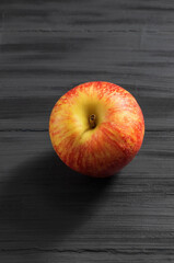 In the center on a black wooden background lies a red apple