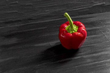 On a wet black wooden table lies a single ripe Bell pepper