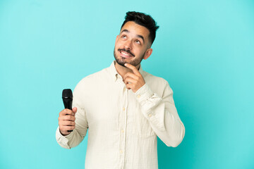 Young caucasian singer man isolated on blue background looking up while smiling