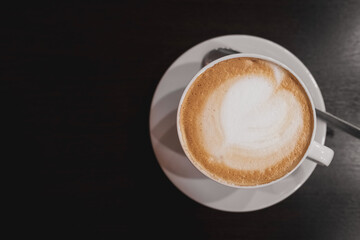 a white cappuccino coffee cup with a heart - shaped pattern on the foam. a cup and saucer on a dark wooden table in a cafe or restaurant