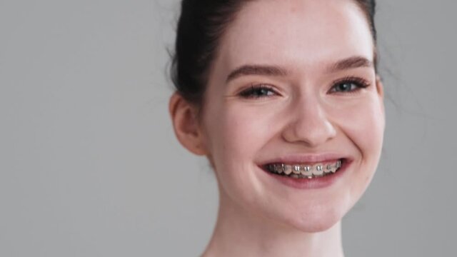 A pleased half naked woman is winking to the camera standing isolated over gray wall in the studio