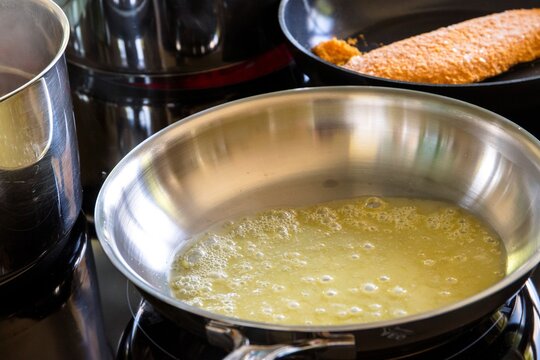 An induction cooker with some stainless steel pans and pots on them. One of the pans has molten fizzy butter in it, so the cook can start frying meat or prepare another type of food in it.