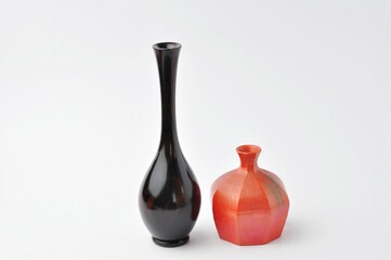 Vase for flowers in orange, low round isolated and tall black leaves on white background.