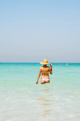 Woman wearing straw hat walking out the water against blue sea background