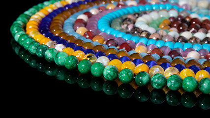 Colorful beaded necklaces are laid out in circles on a black background with reflection. Isolated jewelry made from natural stones, energy mineral, amulet. 