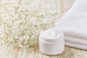 Fototapeta na wymiar Natural face cream or lotion, organic cosmetic product to moisturize the skin with a towel and flowers on the background.
