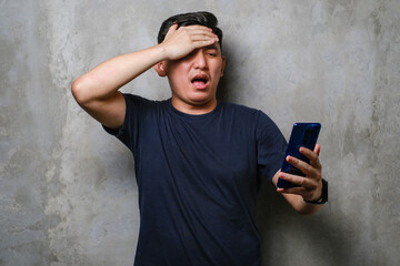 Young Japanese man using smartphone stressed with hand on head, shocked with shame and surprise...