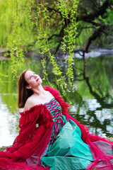 portrait of brunette young woman in red gown sitting by lake