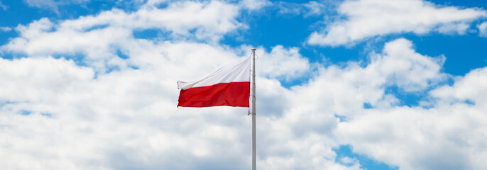 Poland flag waving in the wind in the blue sky. Polish white-red flag in the clouds