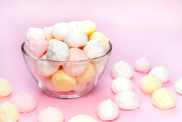 Meringues of pale yellow, white and pink in a transparent vase on the pink background. Selective focus