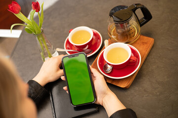 Chroma key phone screen in the hands of a woman drinking tea in cafe