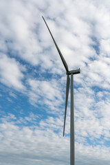 Wind turbine on a green field against a blue sky with clouds.