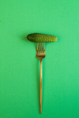 Cucumber  impaled on a gold fork on the green  background. Location vertical.