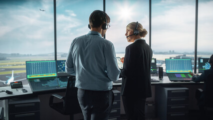 Female and Male Air Traffic Controllers with Headsets Talk in Airport Tower. Office Room is Full of Desktop Computer Displays with Navigation Screens, Airplane Departure and Arrival Data for the Team. © Gorodenkoff
