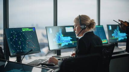 Female Air Traffic Controller with Headset Talk on a Call in Airport Tower. Office Room is Full of Desktop Computer Displays with Navigation Screens, Airplane Departure and Arrival Data for the Team.