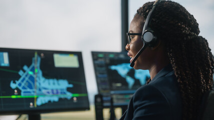 Female Air Traffic Controller with Headset Talk on a Call in Airport Tower. Office Room is Full of...