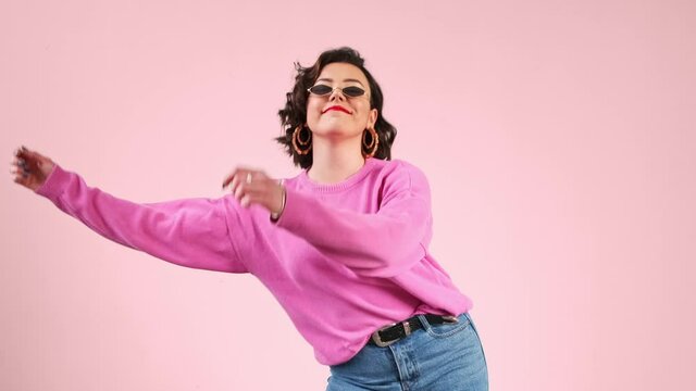 Stylish woman dancing funny trendy meme dance on a pink background. Music concept.