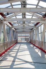Pedestrian crosswalk under glass roof passage in urban environment. Overhead pedestrian bridge overpass in urban area. Footbridge tunnel made from piles and glass with abstract design