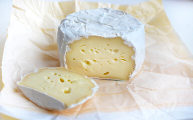 A variety of Brie cheese. Round cheese on white camembert paper, sliced. Fresh Brie cheese. Soft French cheese. Italian food. Milk products.