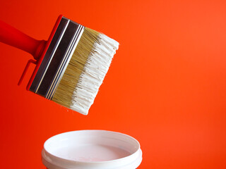 Brush with white paint. White paint dripping from a brush into a jar isolated on a red background. creativity concept.
