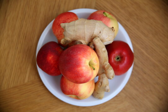 Top view of Delicious red apples and ginger roots, on white plate, with striped wooden background