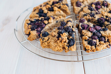 Freshly baked oat blueberry scones on cooling rack on white wooden background. Sweet food with natural ingredients. Vegan gluten free pastry..