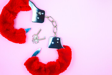 Red sexy fluffy handcuffs with keys on a pink background.