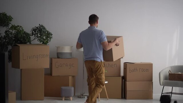 An adult male brings boxes of things into a new house and dances against the background of signed boxes. Real estate and mortgage concept. Minimalism and decluttering