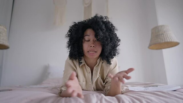 Angry nervous African American woman gesturing talking looking at camera lying on bed. Web camera POV portrait of anxious troubled young manager arguing online from home office