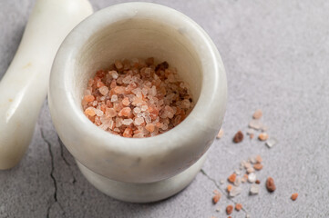 Close-up pink Himalayan salt in a mortar for seasoning on a marble background, top-side view, close-up