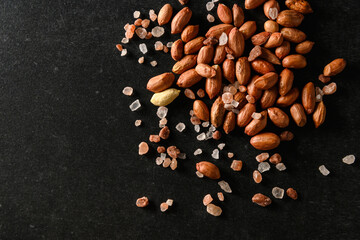 peanuts, dry groundnuts, with Himalayan coarse salt on a dark gray background, top view, empty space for text