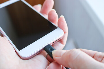 Woman plugging a USB cable into a smartphone connector to charge. Special charging connector for phone.