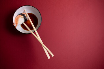 Prawn sushi inside a plate of sauce with two chopsticks around it.