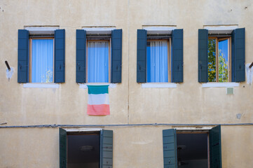 italian flag hanging from arched shuttered window on Venice street
