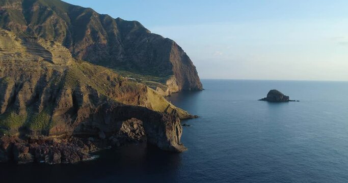 Aerial view of Salina coast, deep cliff, little village in a summer sunset. Blue sea, sky and wind for a peaceful moment. Road cross the valley, huge mountains in the background