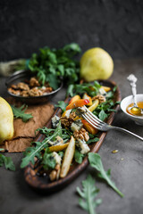 Salad with gorgonzola, rucola, pears, walnuts and honey in a long  wooden plate. Healthy eating. Cheese with a noble blue mold on a gray table and
dark background. Healthy eating. Light dinner.