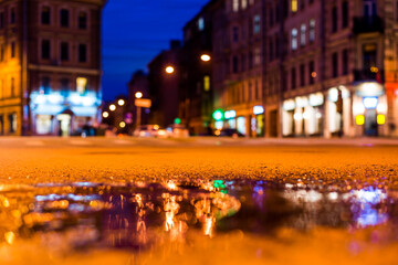 Obraz premium Nights lights of the big city, the empty night crossroad between buildings. Close up view of a puddle level