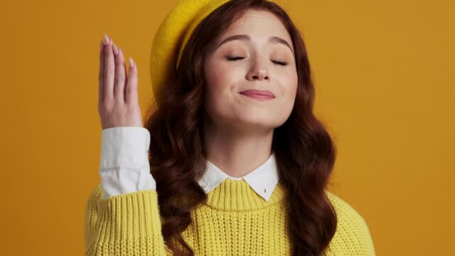 A portrait of a smiling woman showing a bellissimo gesture while standing in a yellow studio