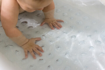 Young baby on hands and knees in bathtub; clear bath mat with suction cups used to prevent...