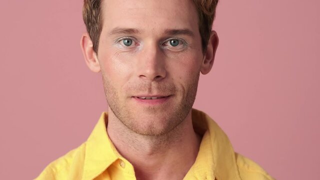 The close-up view of a smiling man with makeup looking to the camera in a pink studio