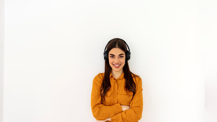 Cropped shot of an attractive long haired woman listening to music while standing against a grey background in studio. Happy young Caucasian woman in headphones listening to music over grey background